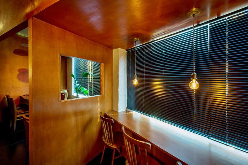 Dining counter with plywood partition and black horizontal blinds lit by pendant bulbs at dusk