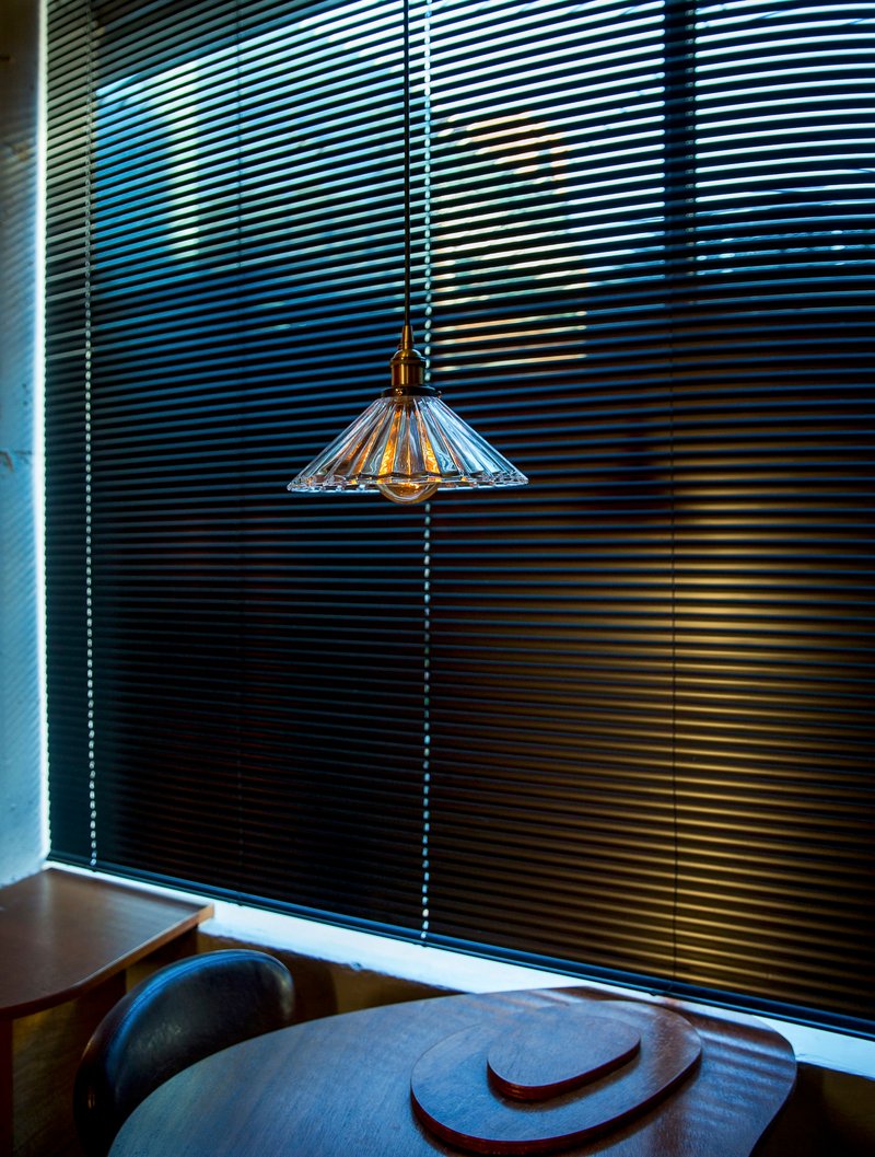 Ribbed glass pendant lamp hanging before black metal blinds with afternoon light filtering through