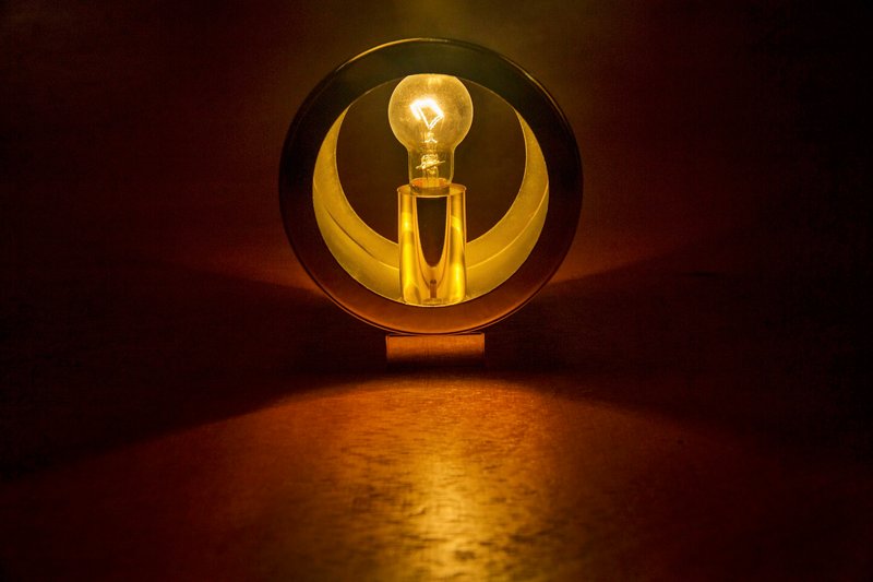 Circular brass portal framing an illuminated bulb above a timber floor in low light