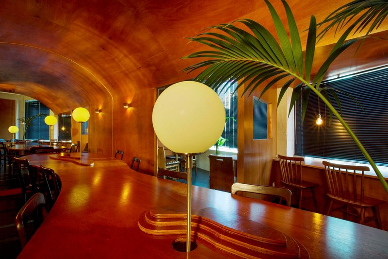 Interior dining space with laminated wood vault ceiling and spherical pendant lamps at twilight