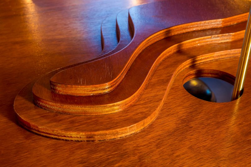 Close-up of layered plywood table edge with flame-shaped cutout against the timber floor