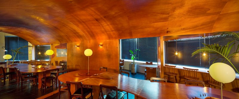 Wide view of the dining hall showing the vaulted timber ceiling and window bays at evening