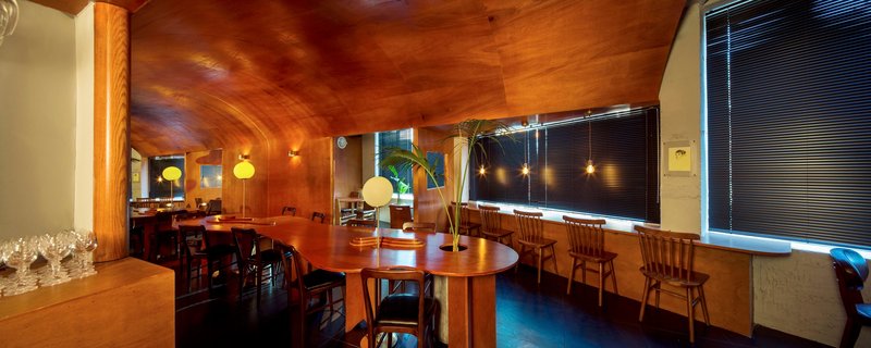 Panoramic view of dining hall with vaulted plywood ceiling and blinds along the window wall