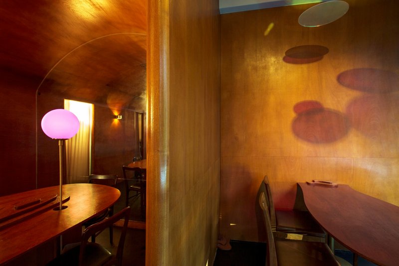 Arched plywood corridor with pink globe lamp and colored shadows cast on the wall