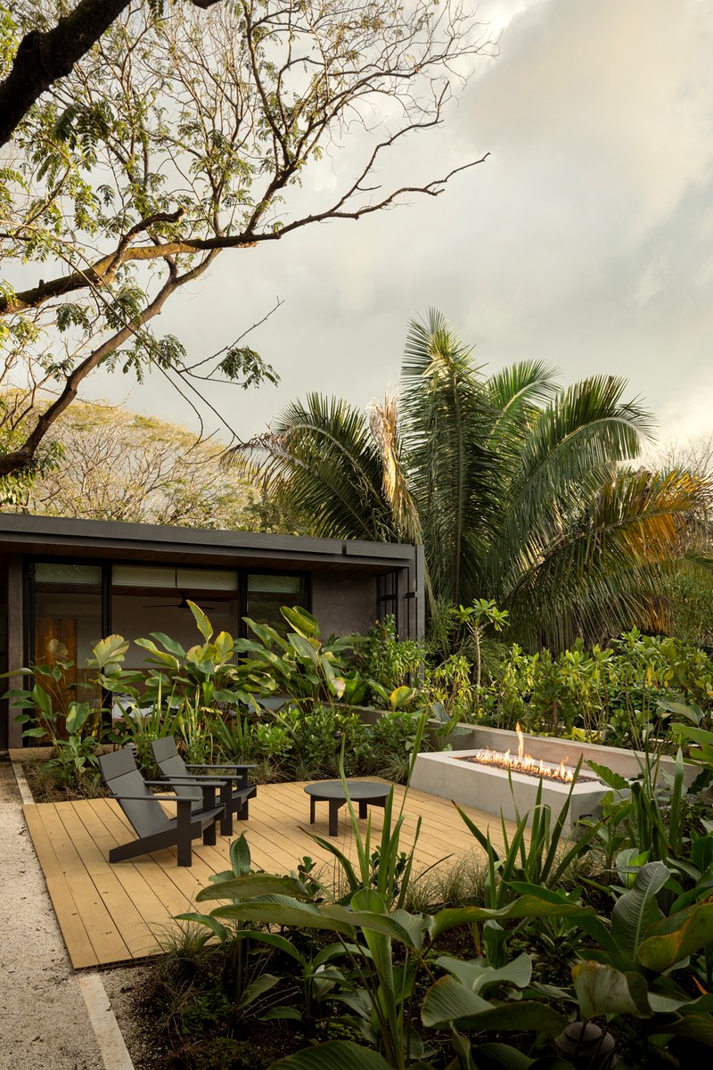 Timber deck terrace with fire feature and lounge chairs amid planted beds under overcast sky
