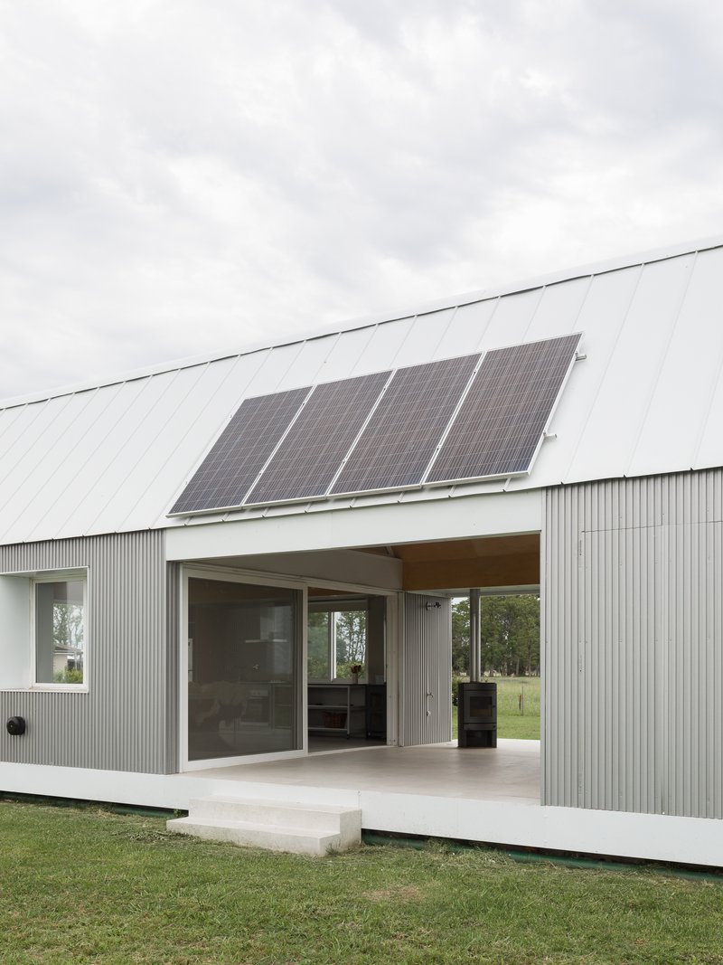Concrete terrace and sliding doors beneath metal roof with four mounted solar panels