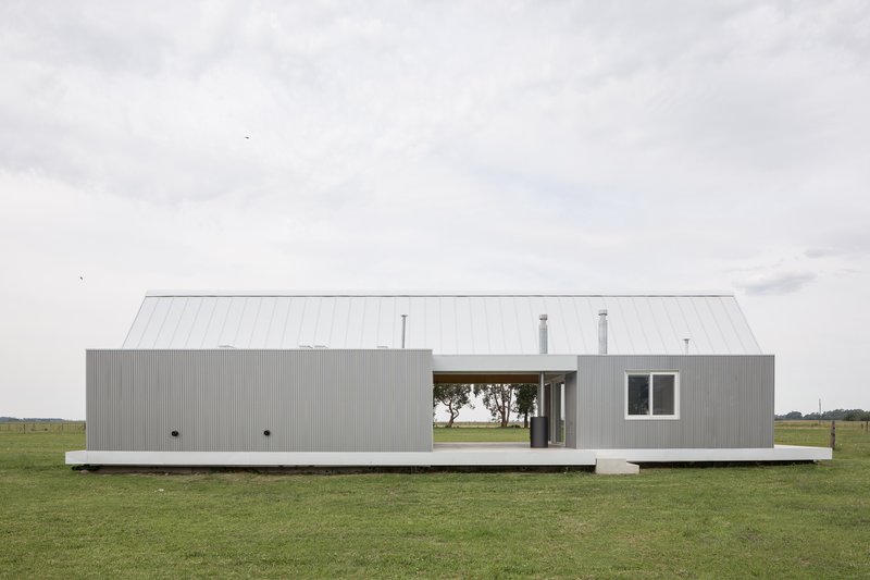 Long side elevation of corrugated metal volume on concrete plinth in grassy field