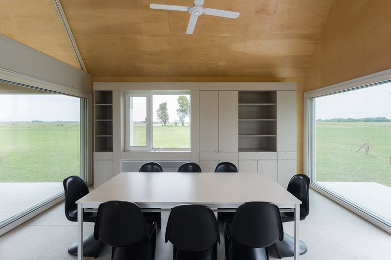 Dining table with black chairs beneath plywood ceiling and built-in cabinetry with views to pasture