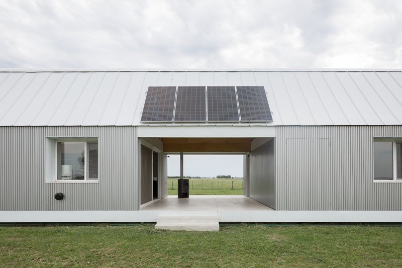 Corrugated metal facade with central breezeway passage and solar panels on the gabled roof