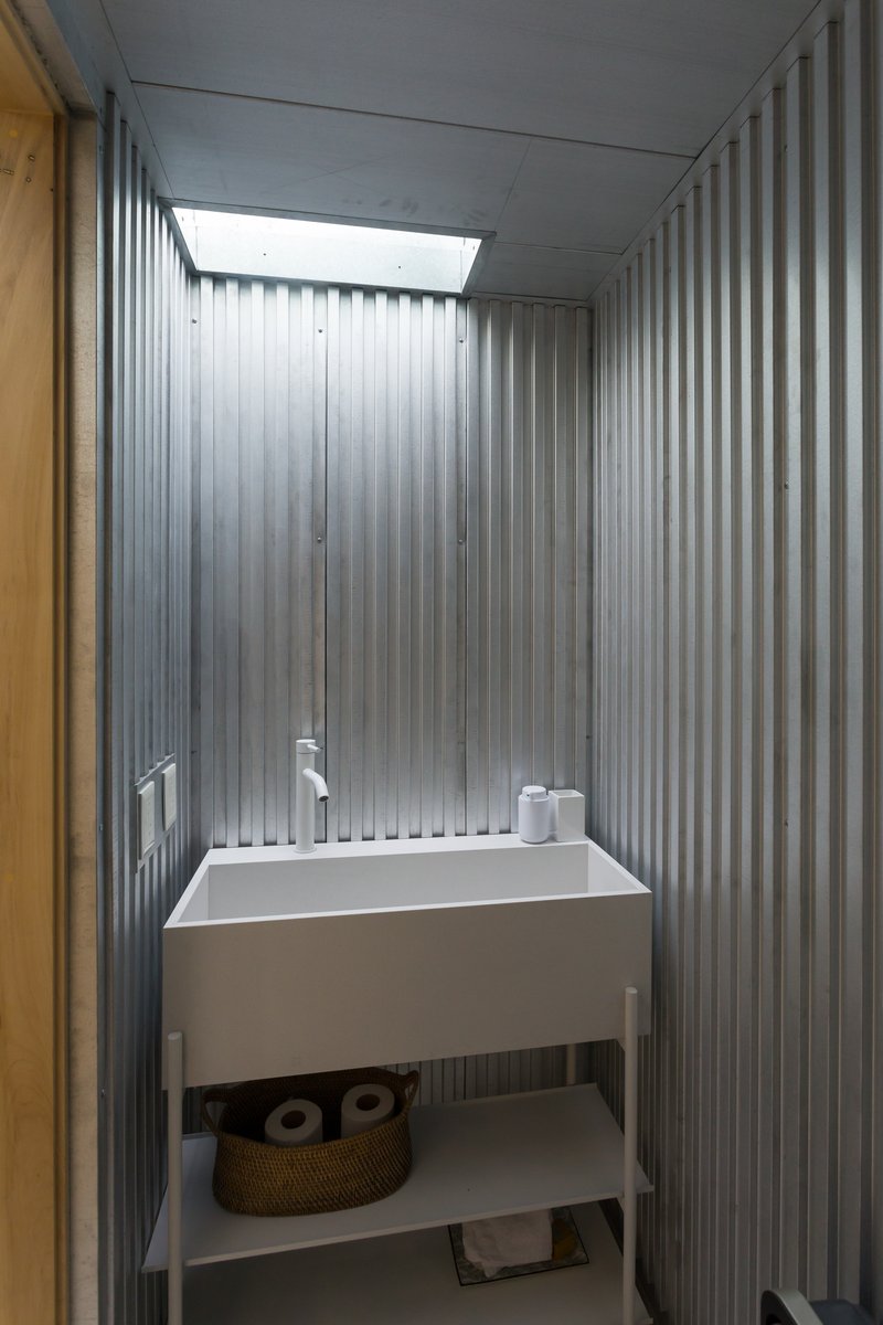 Small bathroom with white sink console and corrugated metal walls lit by a rectangular skylight
