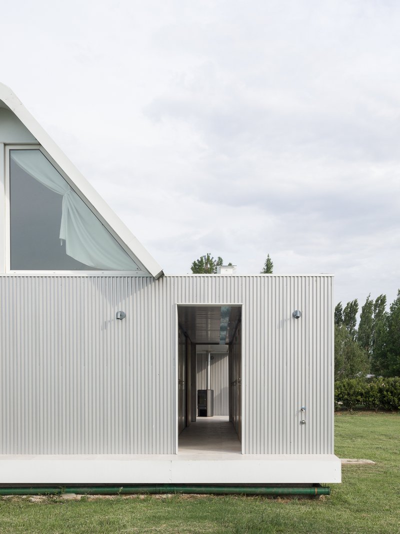 Vertical corrugated metal facade with a central doorway framing a view through to an interior corridor
