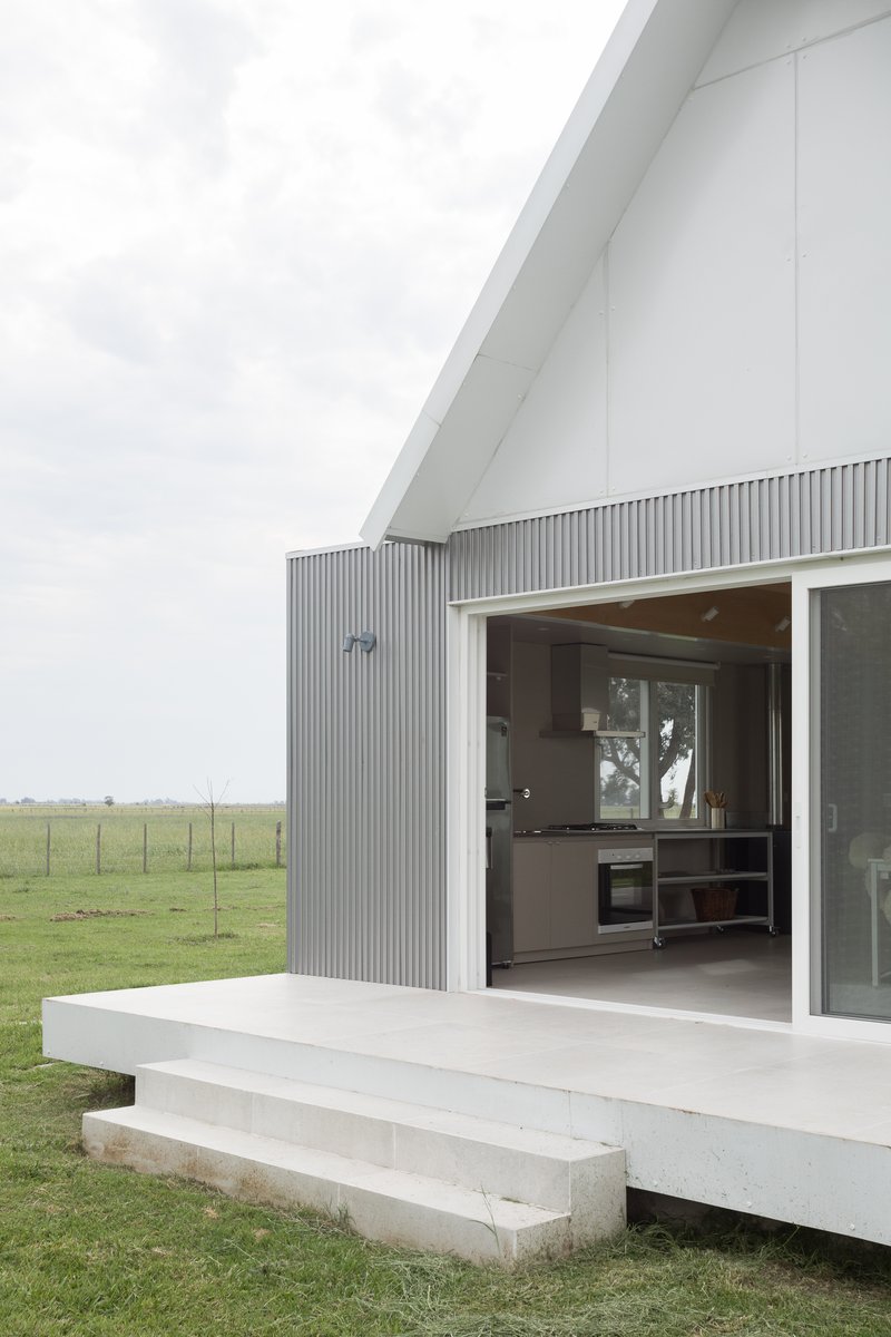 Open glass sliding doors revealing a kitchen inside, with a white terrace and concrete steps