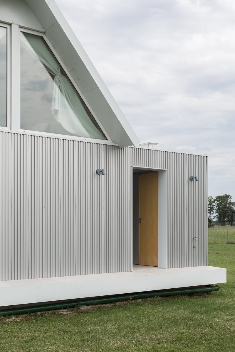 Facade view showing the angled glazed window above the corrugated metal volume on a raised terrace