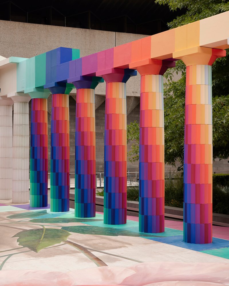 Close-up of the multicolored cylindrical columns supporting the stepped rainbow beam against a concrete backdrop