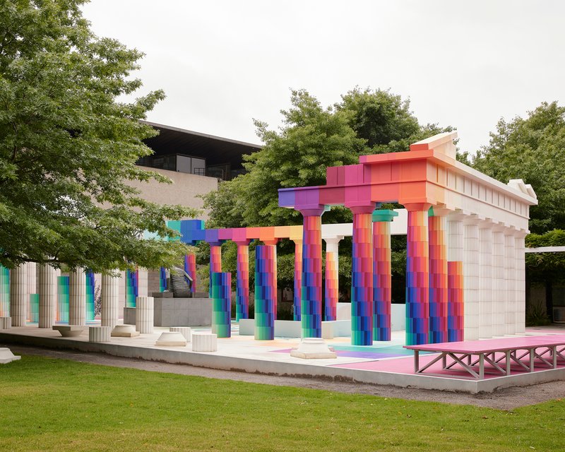 Colonnade structure with multicolored tiled columns and stepped entablature framed by lawn and surrounding greenery