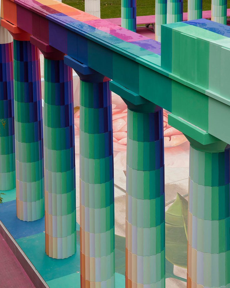 Close-up of pixelated cylindrical columns supporting gradient-striped beams beneath a clear sky