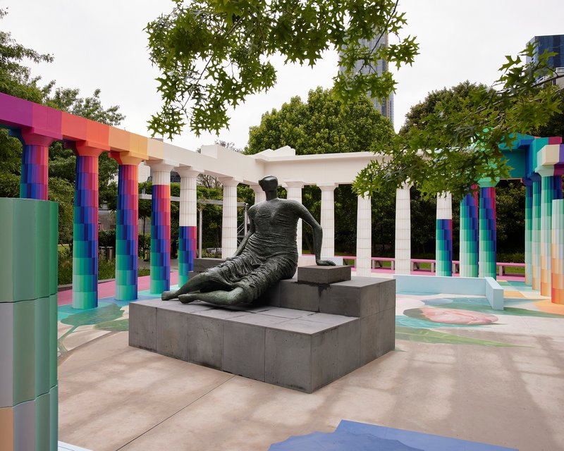 Bronze sculpture on grey plinth surrounded by gradient columns and white entablature on an overcast day
