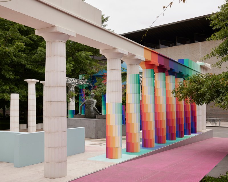Side view of the colonnade with gradient columns and white pillars flanked by mature trees