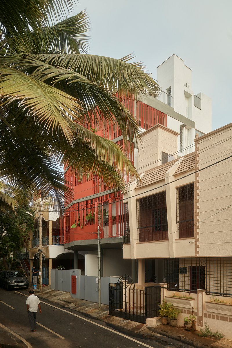 Streetscape view showing the red screened volume rising above neighboring buildings framed by palm fronds