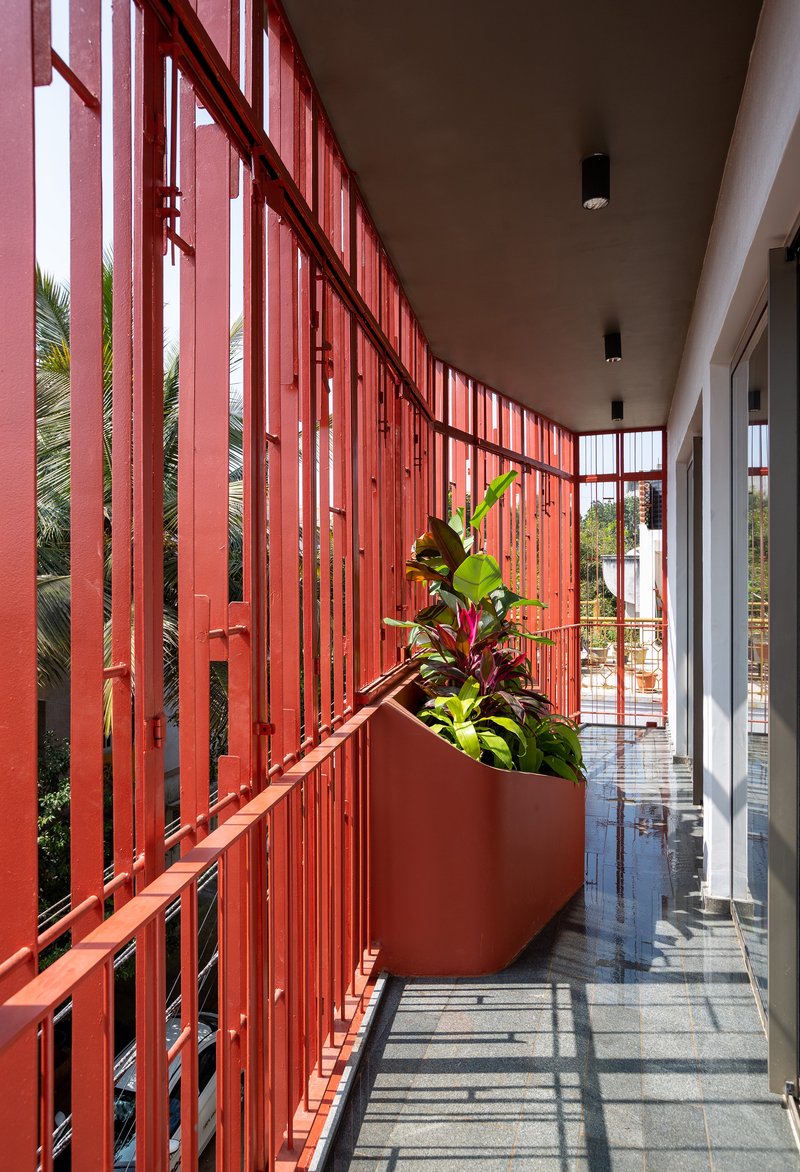 Corridor with red vertical screen wall and planted trough casting shadows on polished stone floor