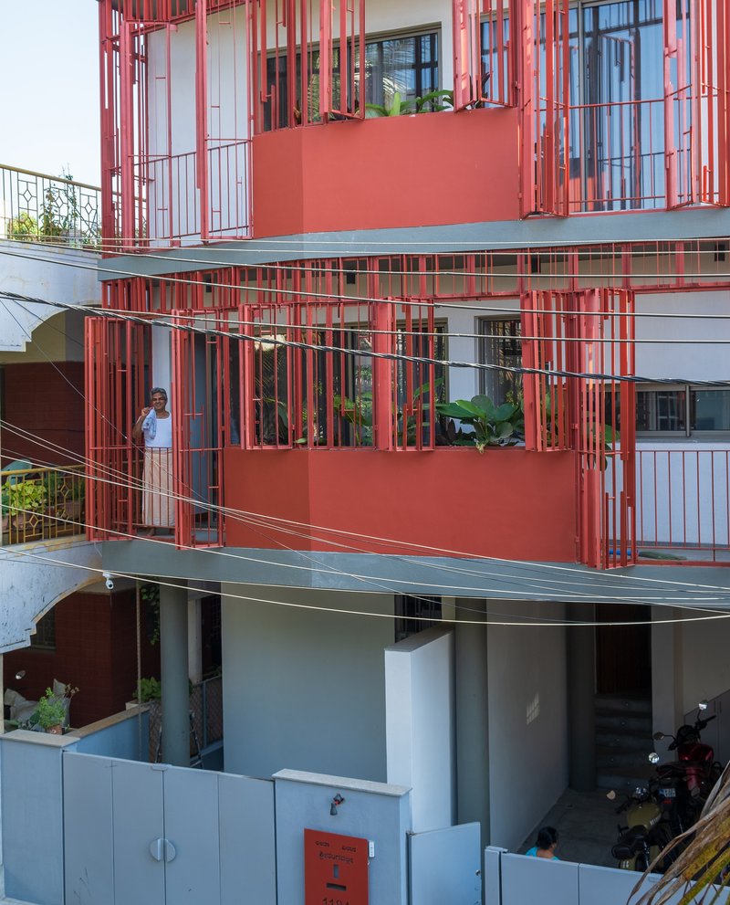 Stacked balconies wrapped in red vertical battens with a resident visible on the upper terrace
