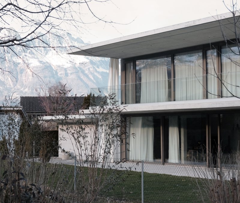 Two-storey concrete and glass facade with deep overhangs framed by bare winter branches and distant mountains
