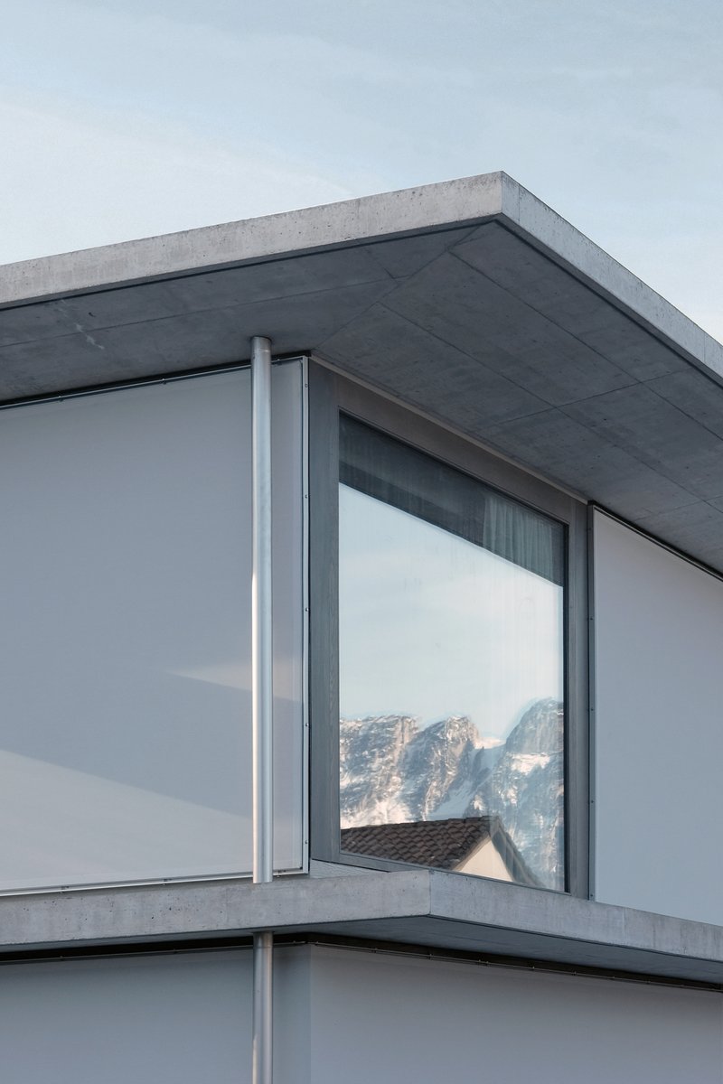 Corner detail of the concrete roof edge and floor-to-ceiling glazing reflecting misty mountain slopes