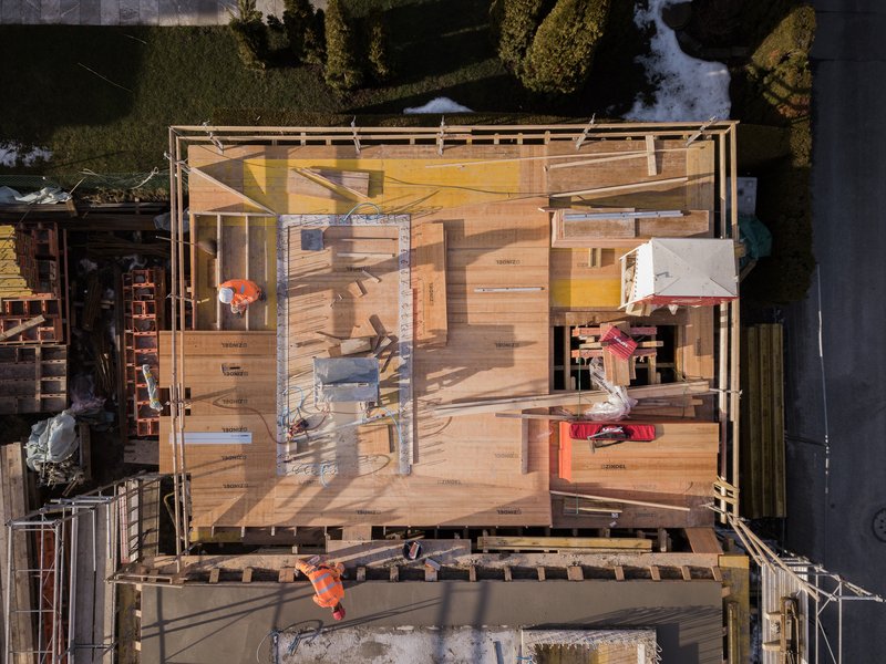 Aerial view of timber-framed structure under construction with workers in orange vests on site