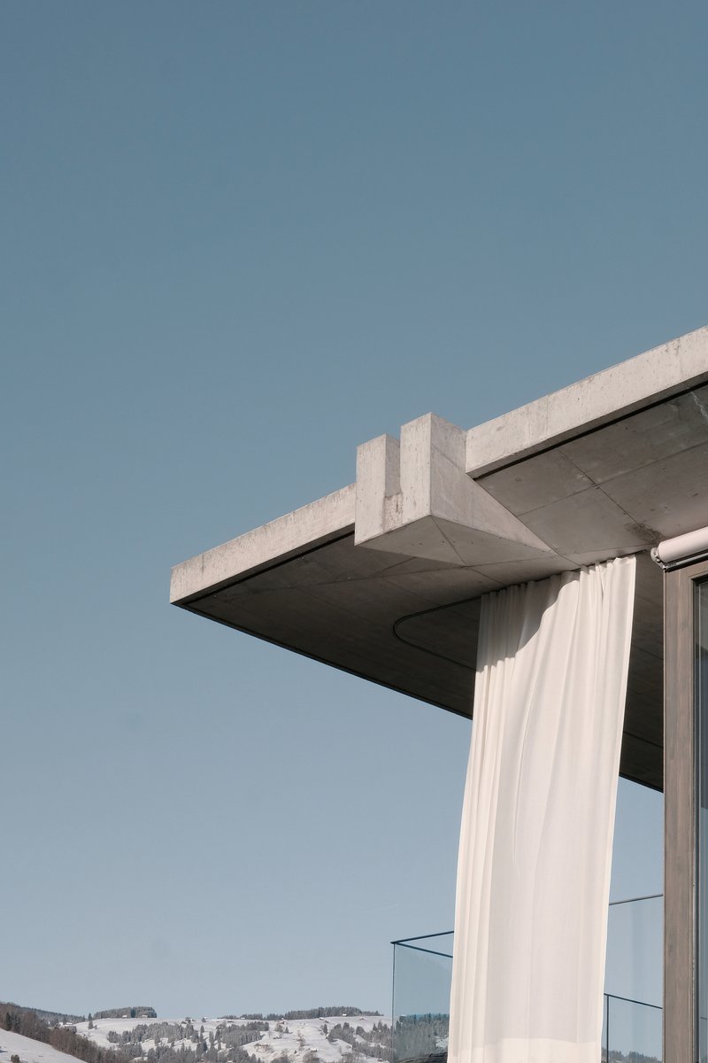Close-up of the cantilevered concrete roof slab with white curtain billowing beside glazed corner