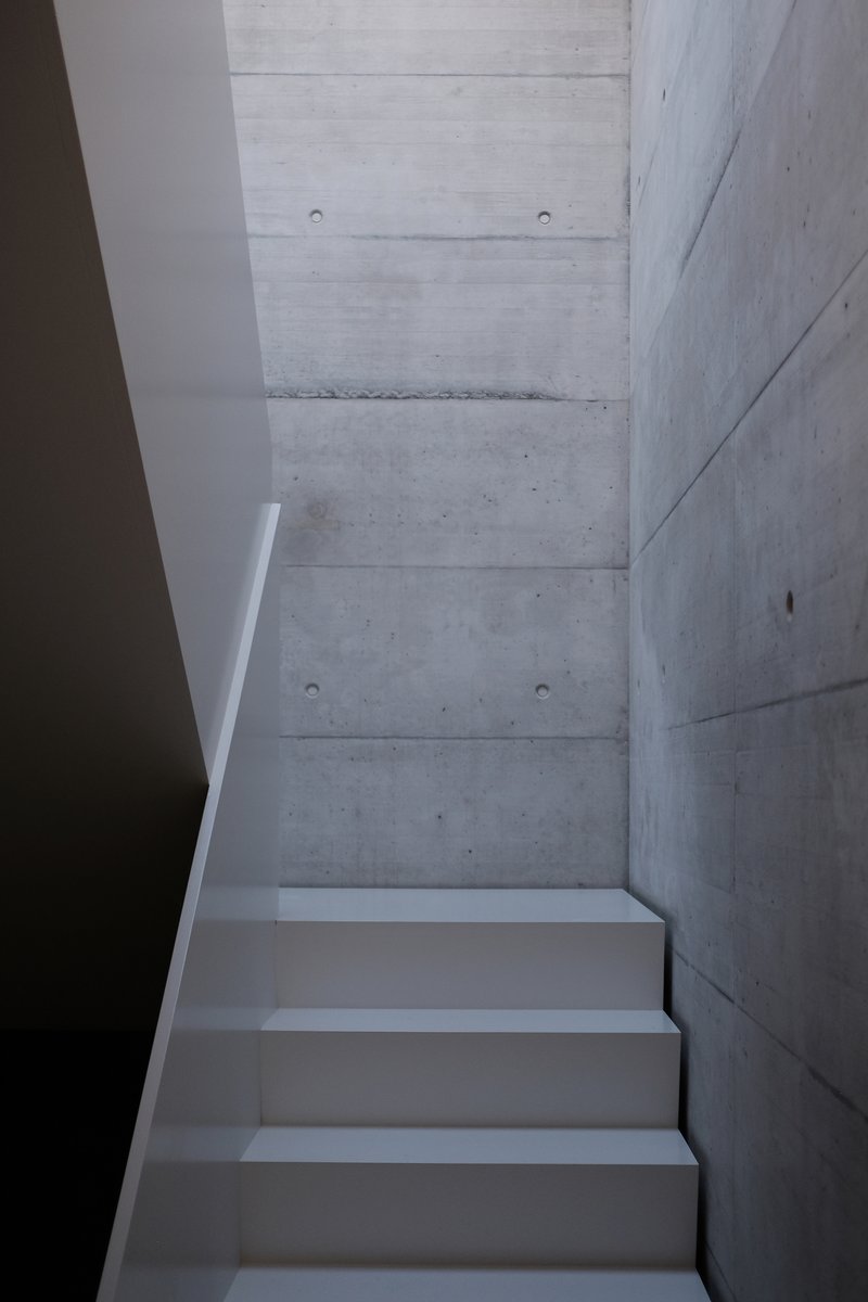 White plastered staircase ascending alongside board-formed concrete walls with visible tie holes
