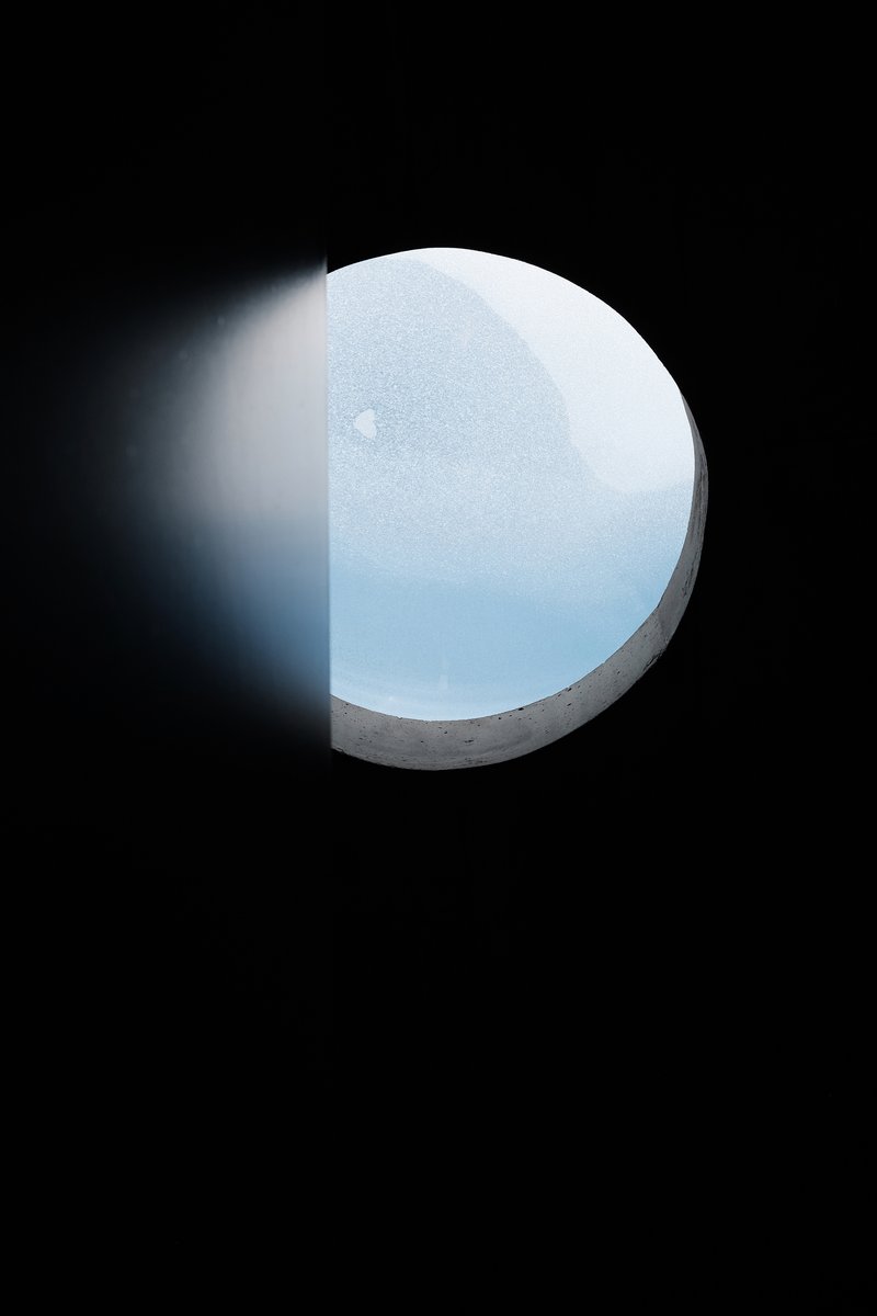 View through a circular concrete skylight opening showing snowfall against a pale grey sky