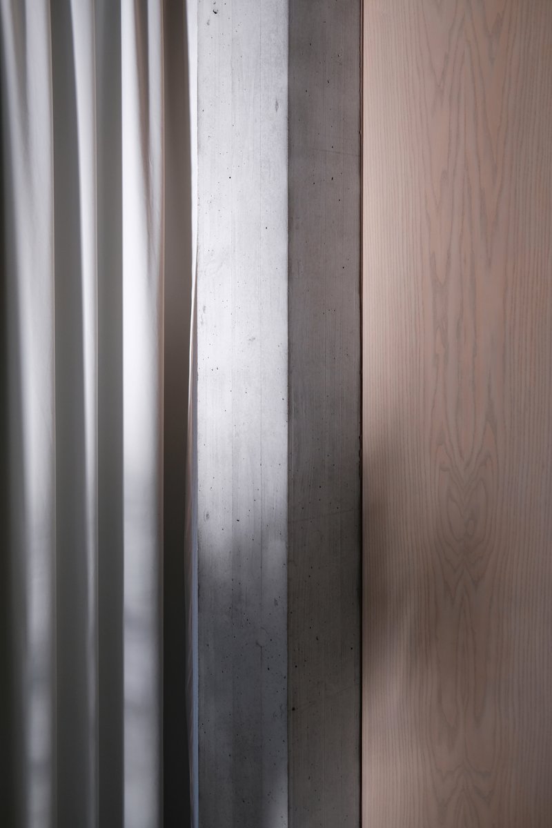Close-up of white fluted paneling meeting exposed concrete column and pale wood veneer surface