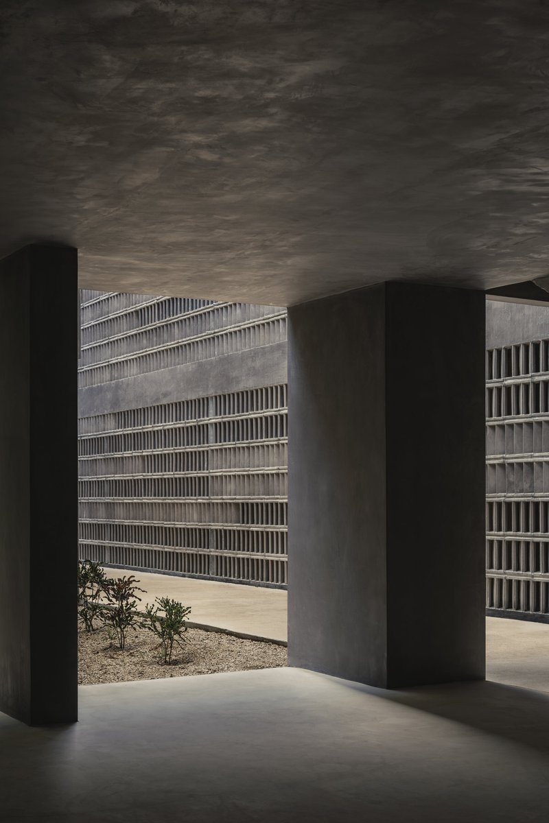 Covered entry passage with dark concrete columns framing views to the courtyard and perforated screen walls