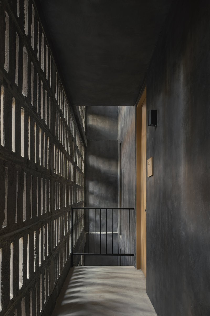 Interior corridor with perforated brick wall catching dramatic natural light beside a metal railing