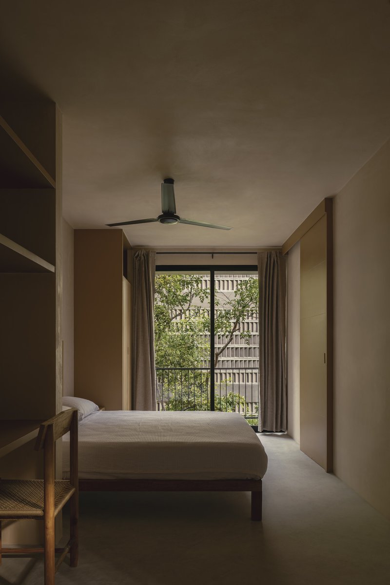 Bedroom with timber bed and ceiling fan facing a glazed door overlooking the perforated screen courtyard