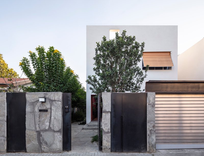Street facade with stone-clad entry wall and black steel gate framing the white volume beyond