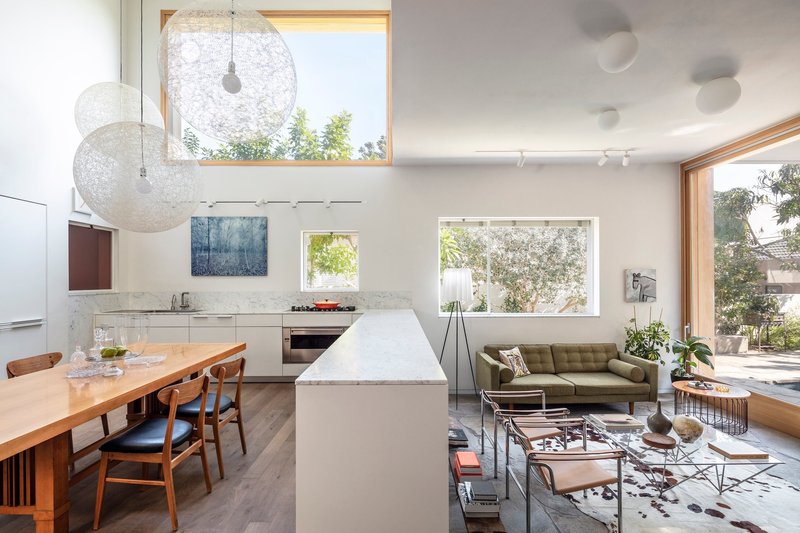 Open plan living space with white kitchen island, timber dining table and timber-framed windows overlooking garden