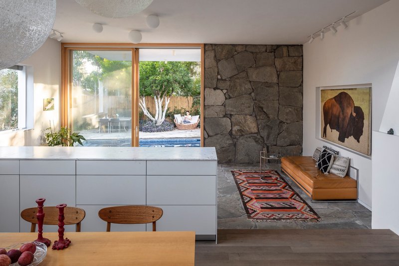 Interior view showing rough stone accent wall beside timber-framed door opening to pool with white-barked tree