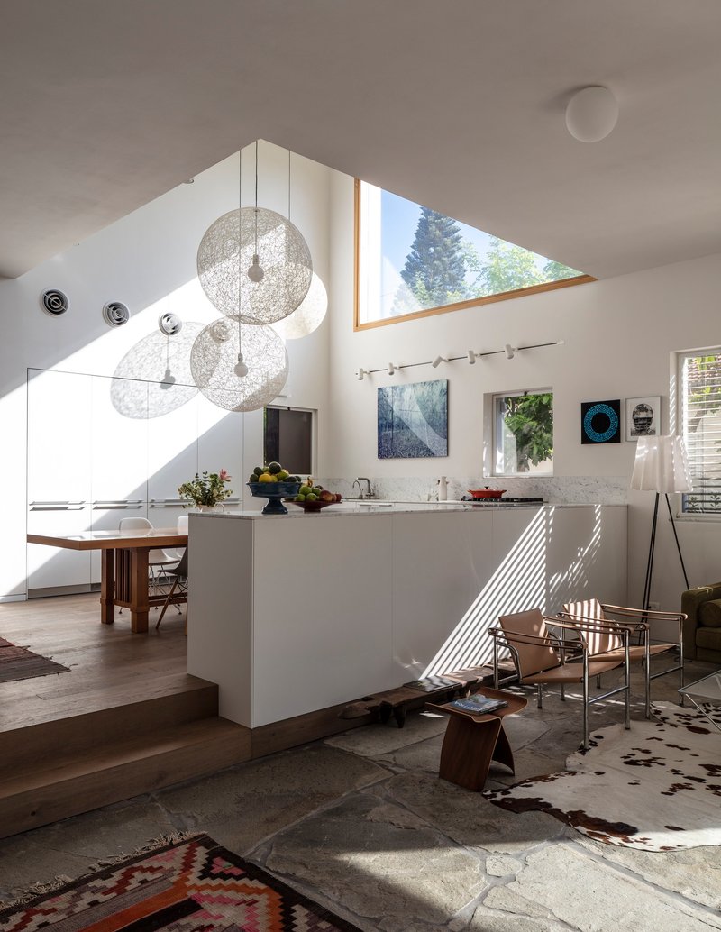 Open kitchen and living area with white island and triangular skylight casting afternoon shadows