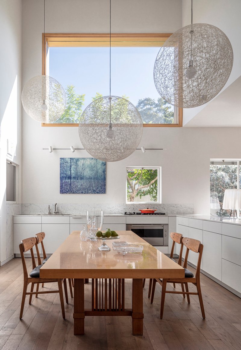 Dining table beneath three spherical pendant lights and timber-framed clerestory window