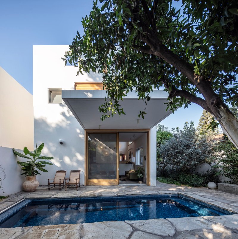 Rear facade with timber-framed glazing opening to the pool courtyard under dappled tree shade