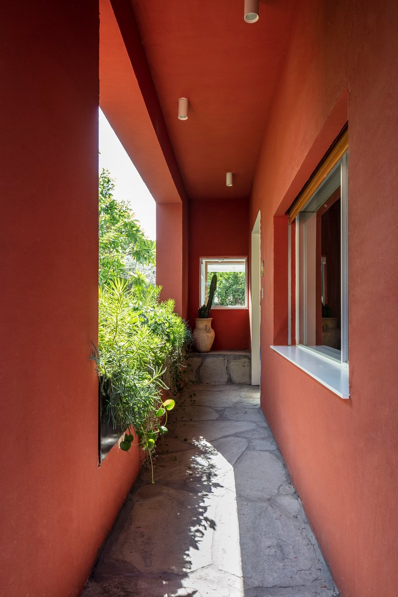 Exterior corridor with terracotta walls and ceiling opening to planted side garden