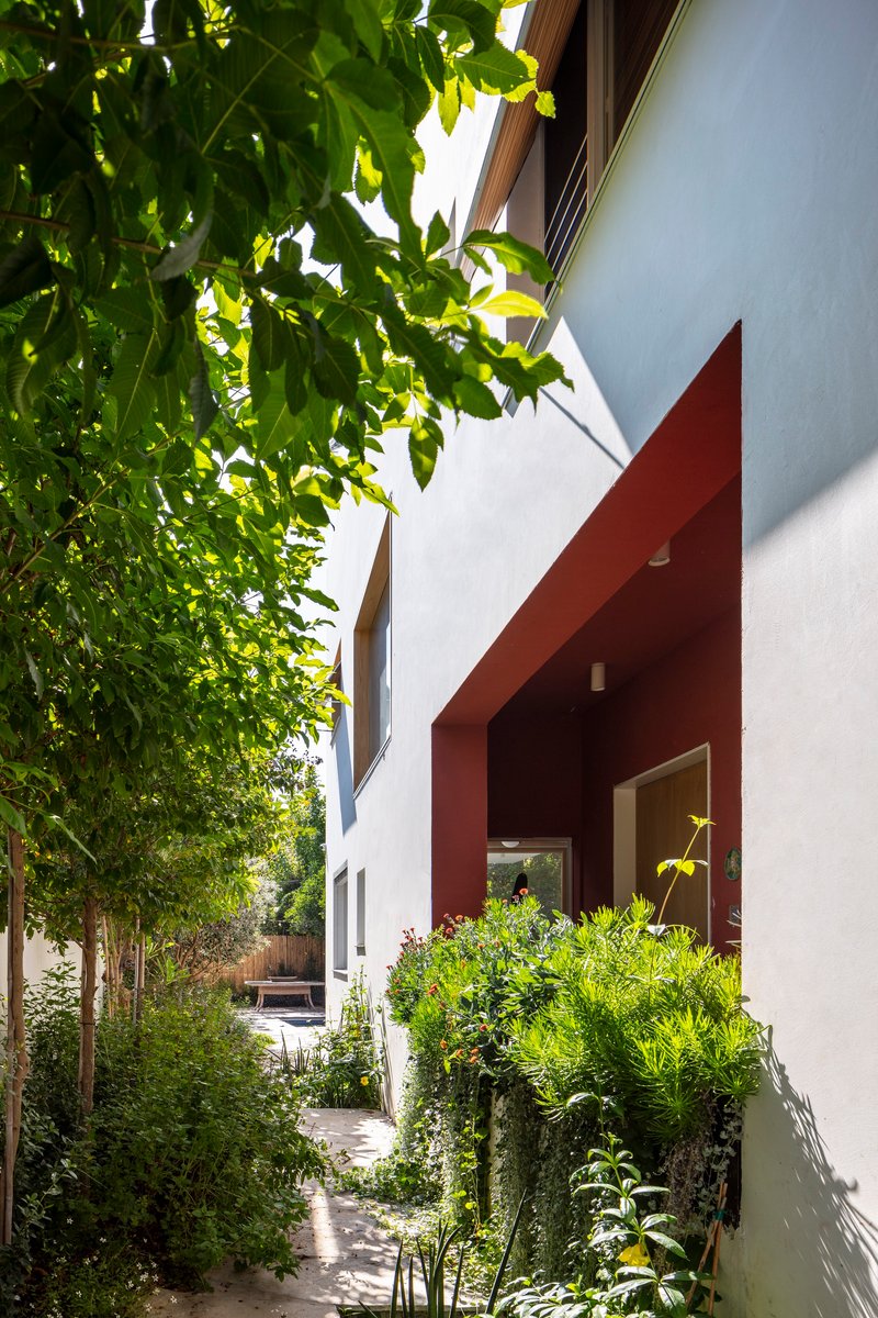 Side passage with red portal frame and white walls beneath overhanging trees in dappled light