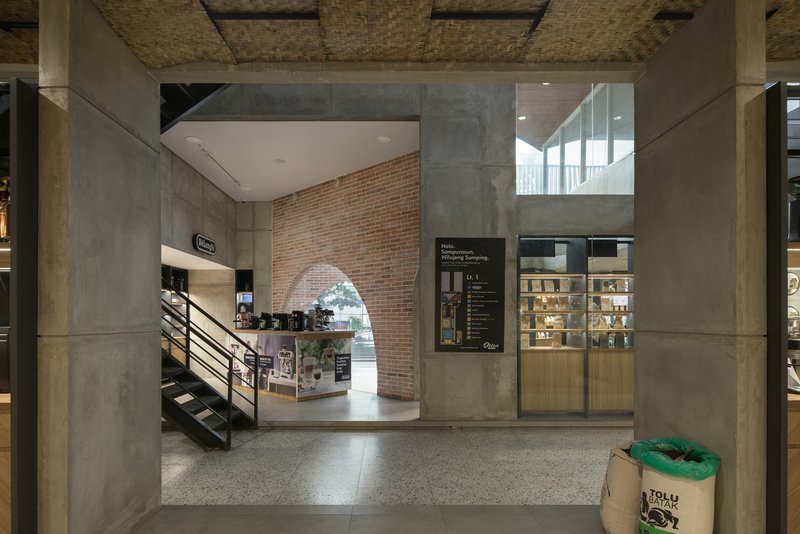 Double-height space with metal staircase leading to mezzanine beneath a woven ceiling panel