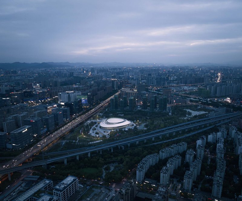 High-altitude view of the building nestled between elevated roads and residential towers at dusk