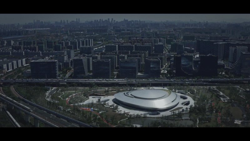 Aerial view of the circular roof amid parkland and urban blocks in afternoon light