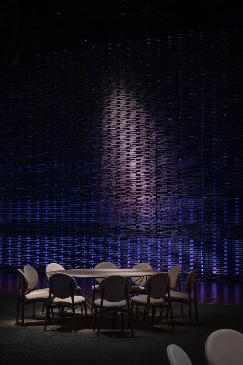 Textured wall installation with vertical relief pattern lit in blue and violet behind a dining table