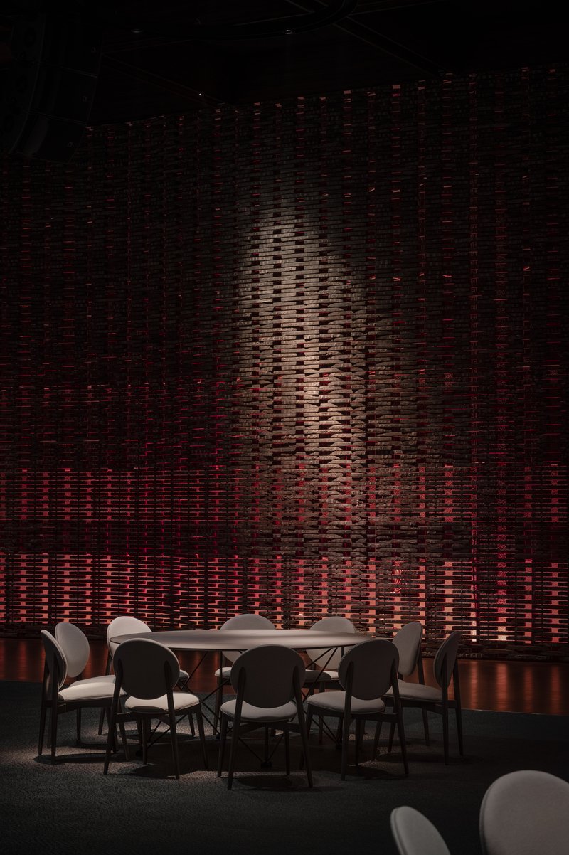 Textured wall installation with vertical relief pattern lit in amber and red behind a dining table