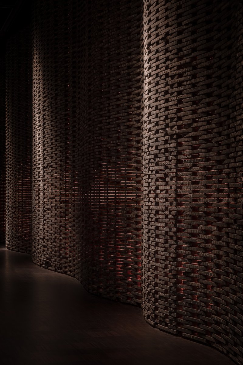 Curving brick wall with basket-weave pattern illuminated by dramatic sidelight in a dark interior corridor