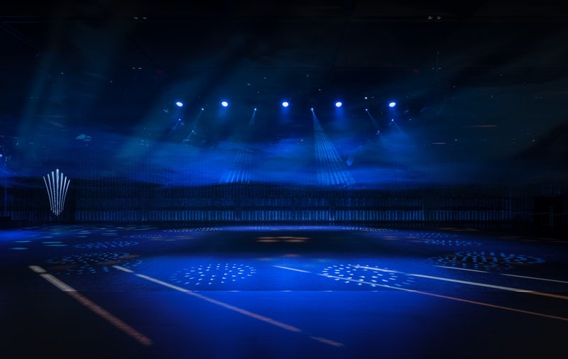 Interior arena space with blue stage lighting and perforated ceiling visible through atmospheric haze